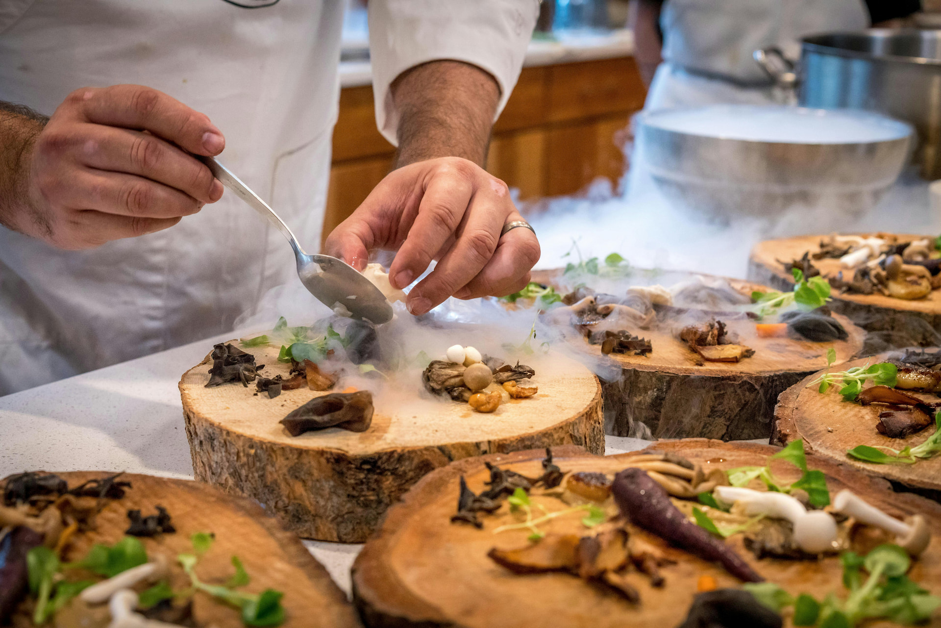 Chef plating gourmet food on wooden boards.