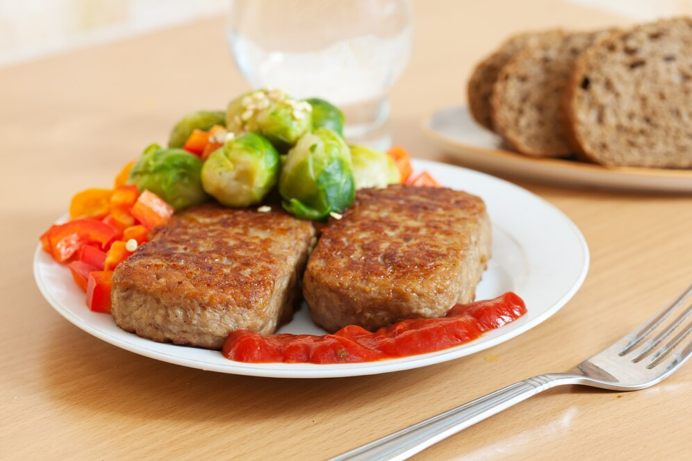 Plant based meat in a plate surrounded by vegetables.